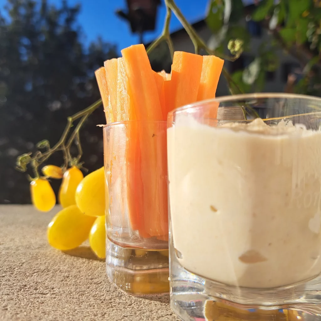 Tempeh Dip mit Creme Fraiche im Vordergrund. Hinten ein Glas mit Karotten und gelbe Tomaten am Zweig.
